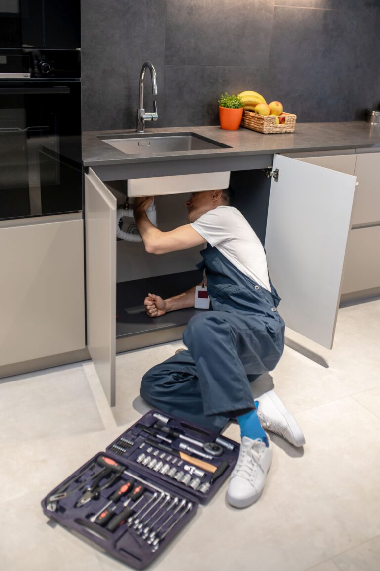 Man with tools peeking under kitchen sink